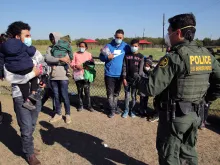 A male Border Patrol agent in La Joya, Texas, speaks in November 2021 with a Honduran man holding his daughter and waiting to be transported to a processing center after turning himself in to seek asylum.
