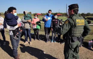 A male Border Patrol agent in La Joya, Texas, speaks in November 2021 with a Honduran man holding his daughter and waiting to be transported to a processing center after turning himself in to seek asylum. Shutterstock