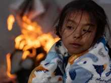 Migrants, including Blaidimar, 8, from Venezuela, warm themselves by a fire outside the U.S.-Mexico border fence while waiting to make asylum claims in El Paso, Texas, on Dec. 21, 2022, as seen from Ciudad Juarez, Mexico.