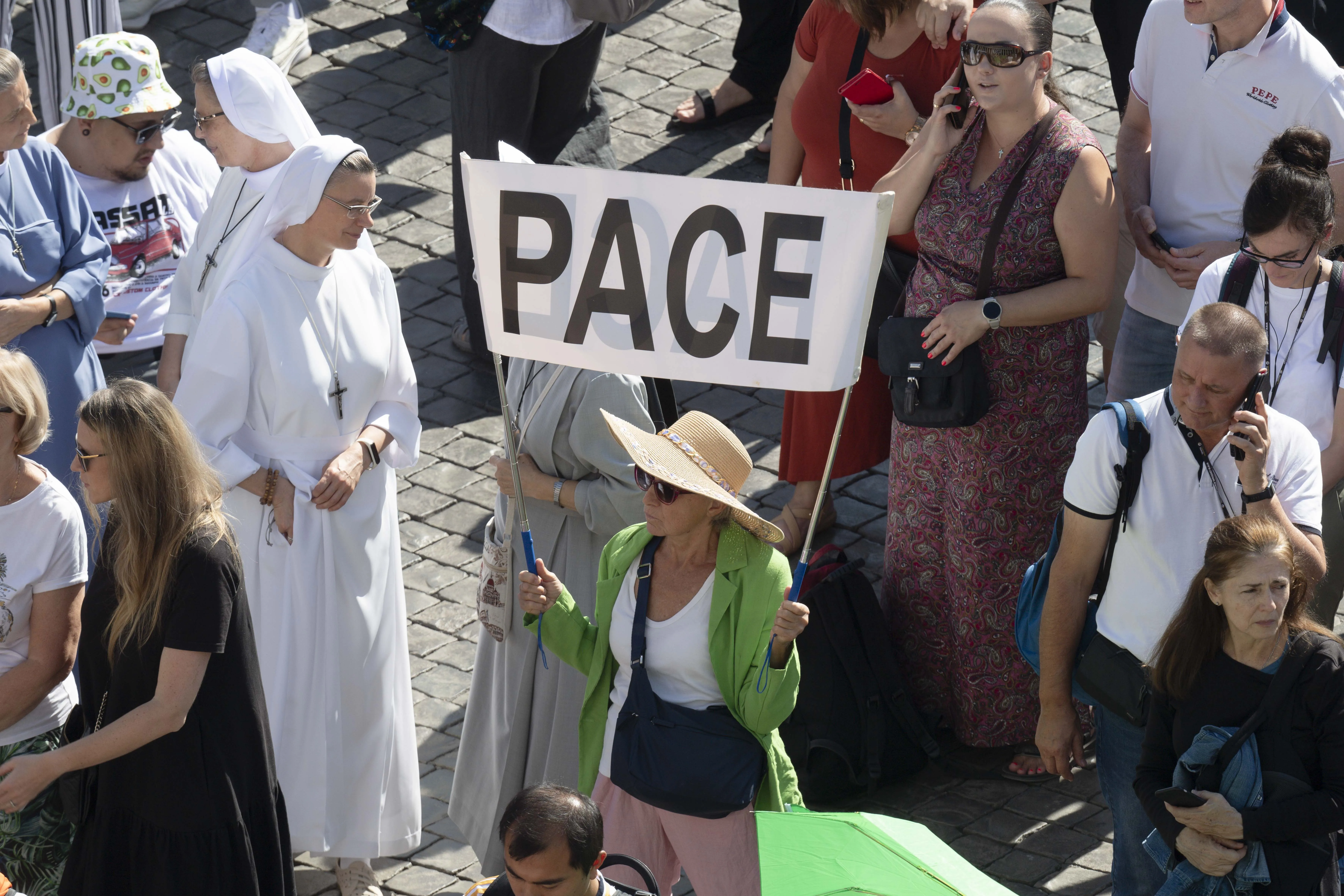 A pilgrim in St. Peter's Square for Pope Francis' weekly Angelus address on Oct. 8, 2023, holds a sign with the word "pace," Italian for "peace.". Vatican Media.