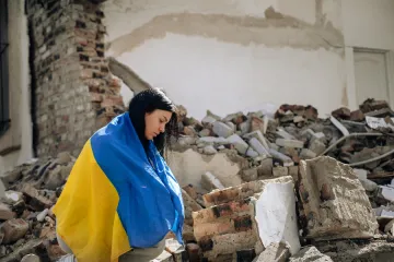 Women with Ukraine flag in front of a destroyed house