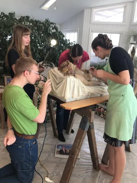 Work progresses on the damaged Christ in Death statue. From left to right: Restoration artists David Loegering, Hanna Loegering, Emily Loegering, and Maria Loh put their newfound skills to work. Credit: New Earth/submitted photo